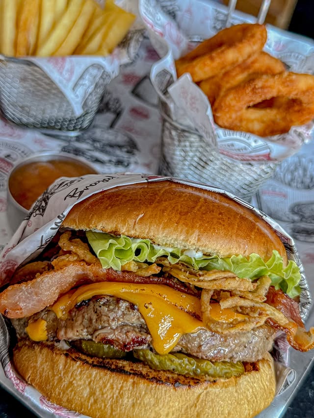 Hambúrguer com bacon e batatas ao fundo